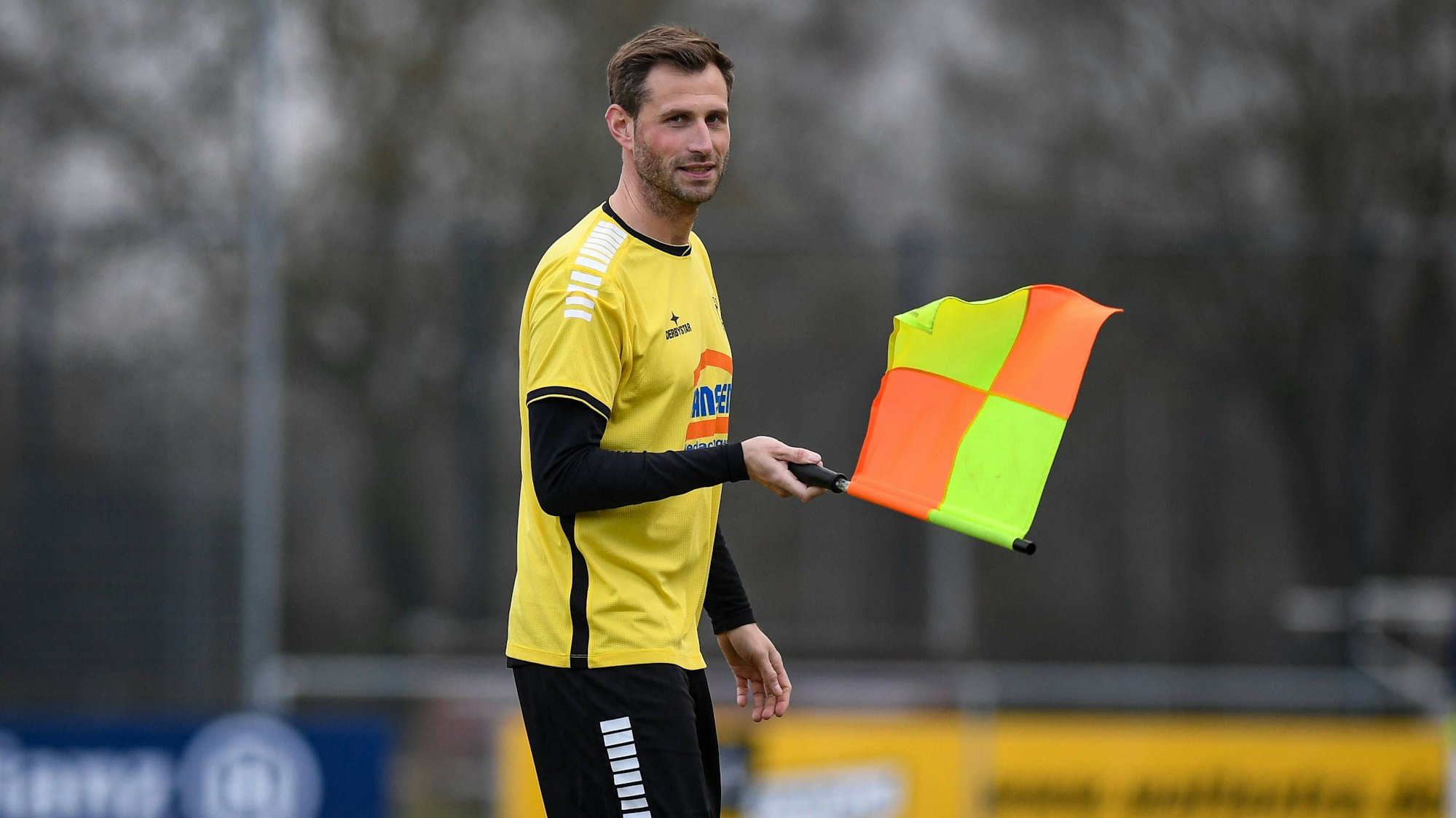 Spielertrainer Sebastian Eul hält bei einem Freundschaftsspiel des SV Siegfried Materborn als Linienrichter eine Fahne in der Hand.