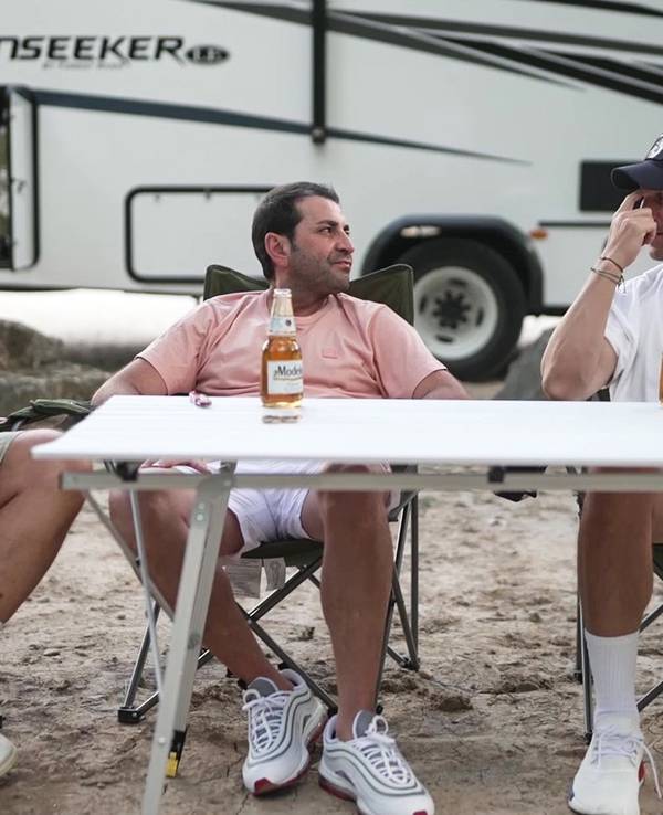 Frank Rosin, Ali Güngörmüş und Alexander Kumptner sitzen an einem Campingtisch vor einem Wohnmobil.