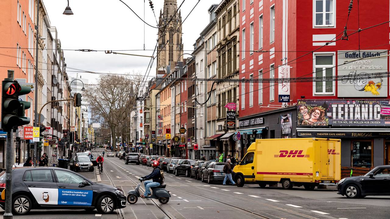 Blick in die Zülpicher Straße in Köln. Neben Autos und einer Vespa ist im Hintergrund ein Kirchturm zu sehen.