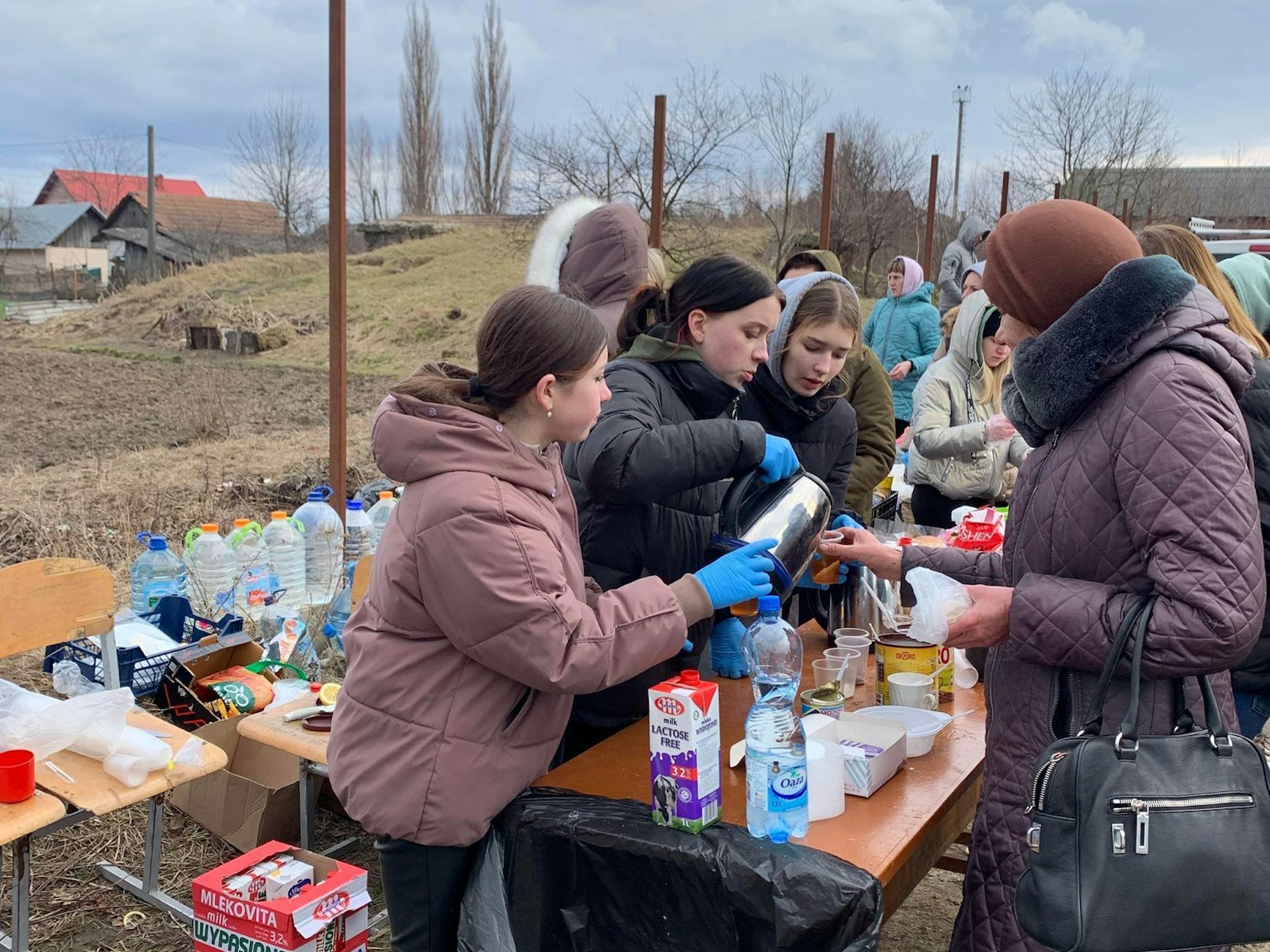 Junge Mädchen schenken warmen Tee für eine geflüchtete Frau ein.
