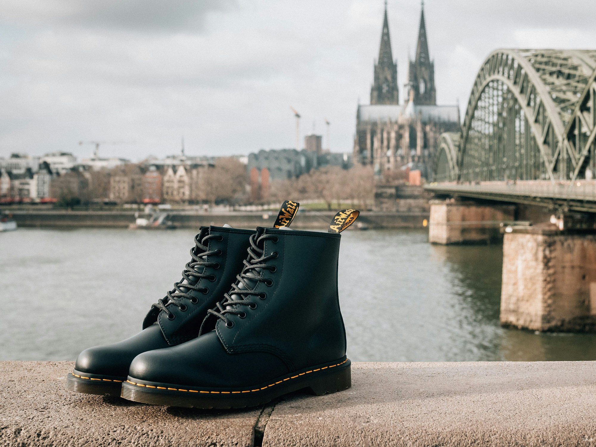 Dr. Martens Schuhe stehen auf einer Mauer. Im Hintergrund befindet sich der Kölner Dom.