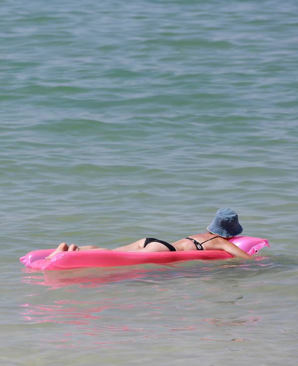Das Symbolfoto zeigt eine Frau im Bikini. Sie trägt einen blauen Hut und liegt bäuchlings auf einer pinken Luftmatratze, die auf dem Meer treibt.