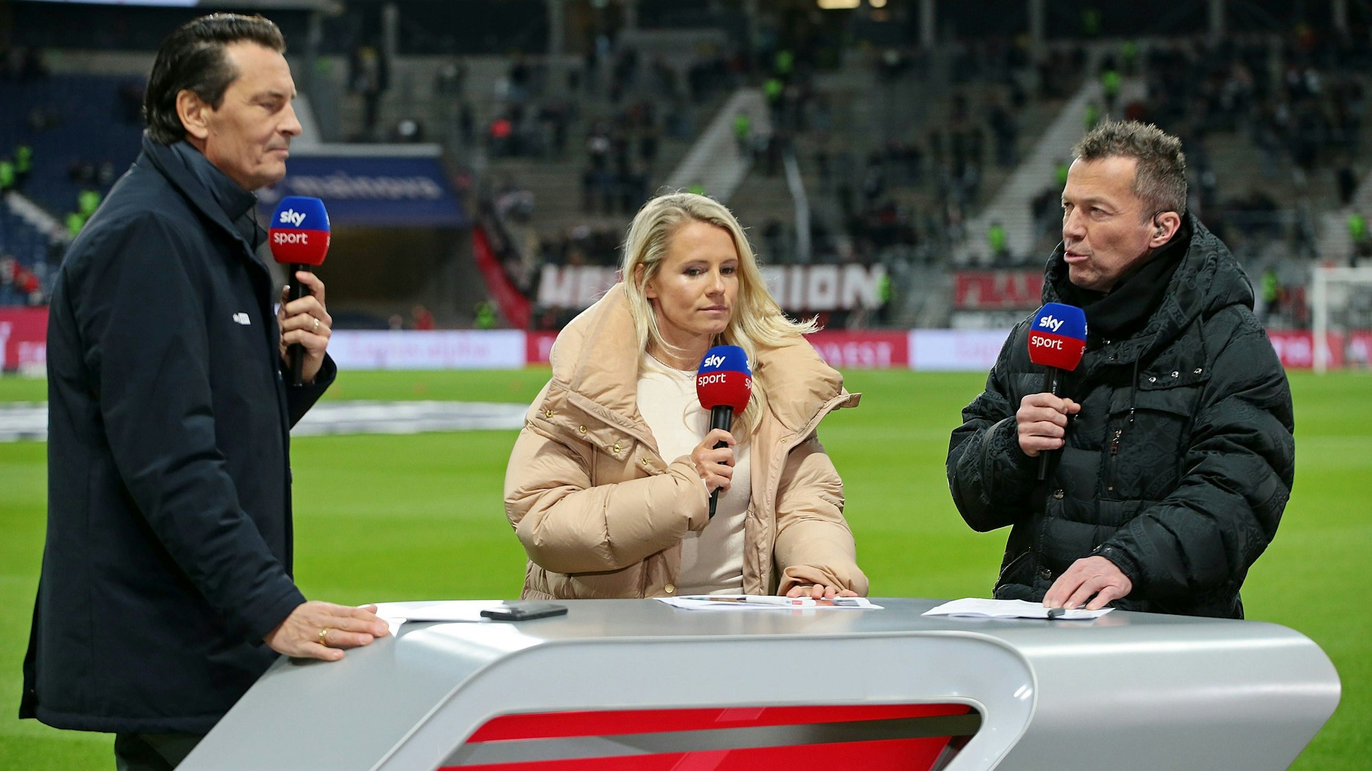 Sebastian Hellmann, Julia Simic und Lothar Matthäus stehen am Sky-Experten-Tisch.
