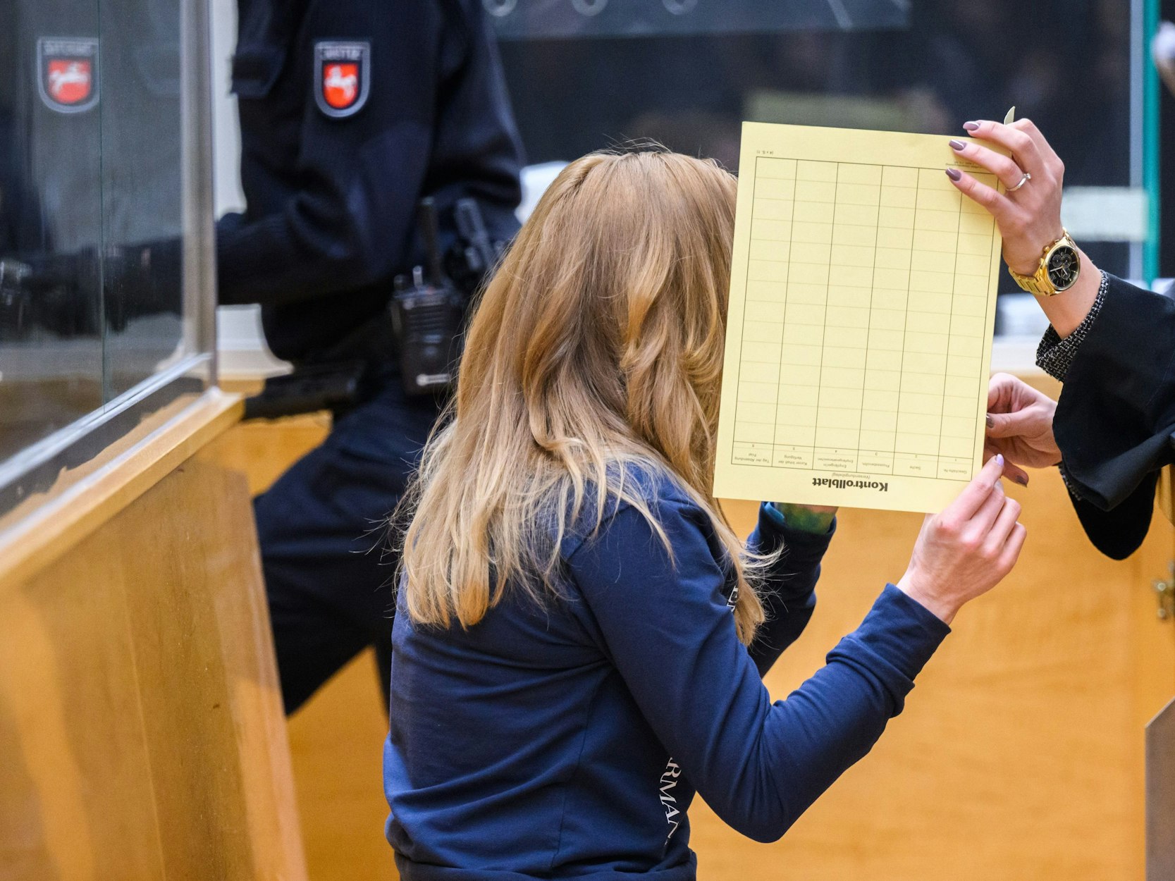 24.02.2023, Niedersachsen, Hannover: Die Angeklagte sitzt mit verdecktem Gesicht im Gerichtssaal im Landgericht. Eine Frau und ein Mann sind wegen Mordes angeklagt, weil sie den Unfalltod von zwei kleinen Jungen verursacht haben sollen. Beiden wird vorgeworfen, sich auf einer Landstraße bei Barsinghausen ein verbotenes Autorennen geliefert zu haben.