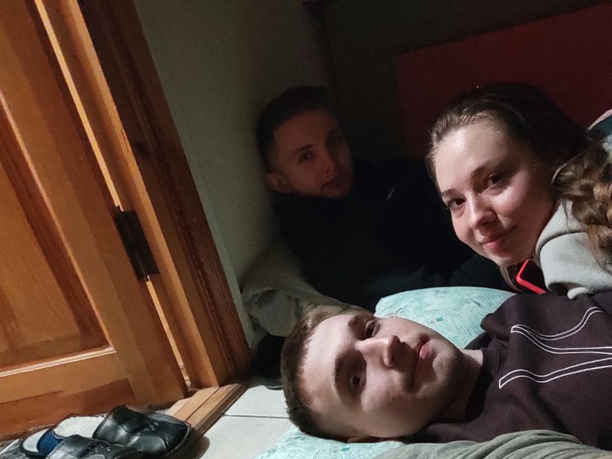 Auf dem Bild sieht man drei junge Menschen, die nebeneinander auf dem Boden liegen und in die Kamera schauen.