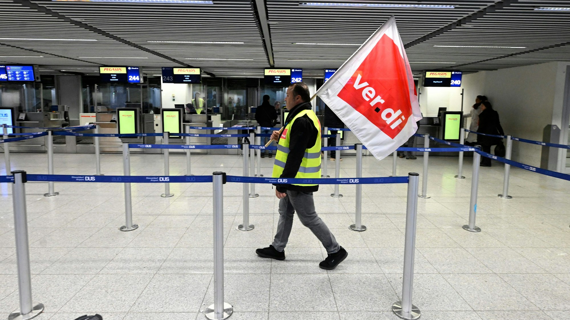 Mann mit Verdi-Fahne geht durch den Flughafen in Düsseldorf.