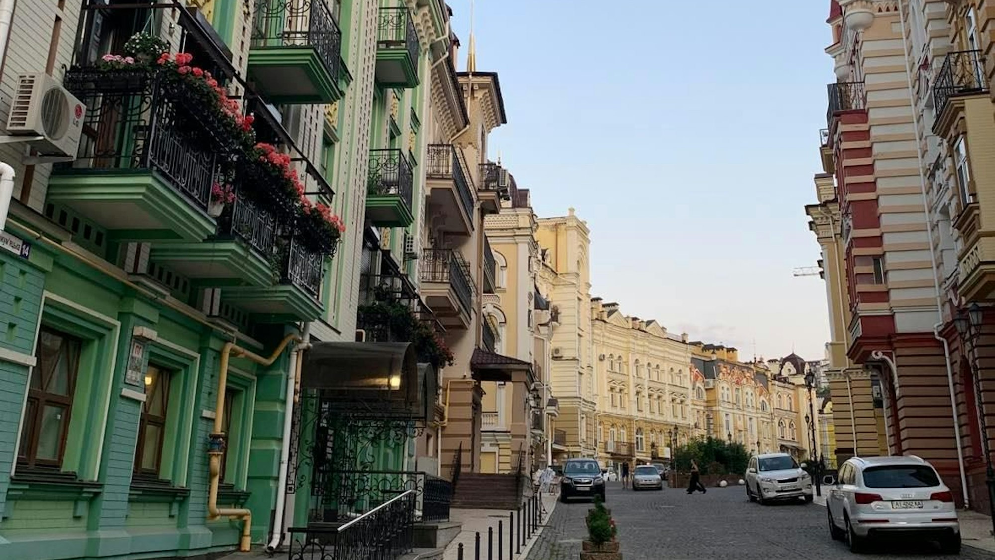 Bunte Fassaden schmücken die Straßen von Kyjiw. Autos sind geparkt, eine Frau überquert die Straße.
