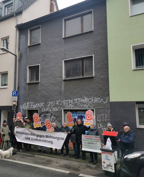 Männer und Frauen haben sich vor einem leerstehenden Haus positioniert. Einige halten ein Transparent mit der Aufschrift „Aktionsbündnis gegen Wohnungsnot und Stadtzerstörung“, andere Plakate mit der Forderung „Mieten Stopp“.