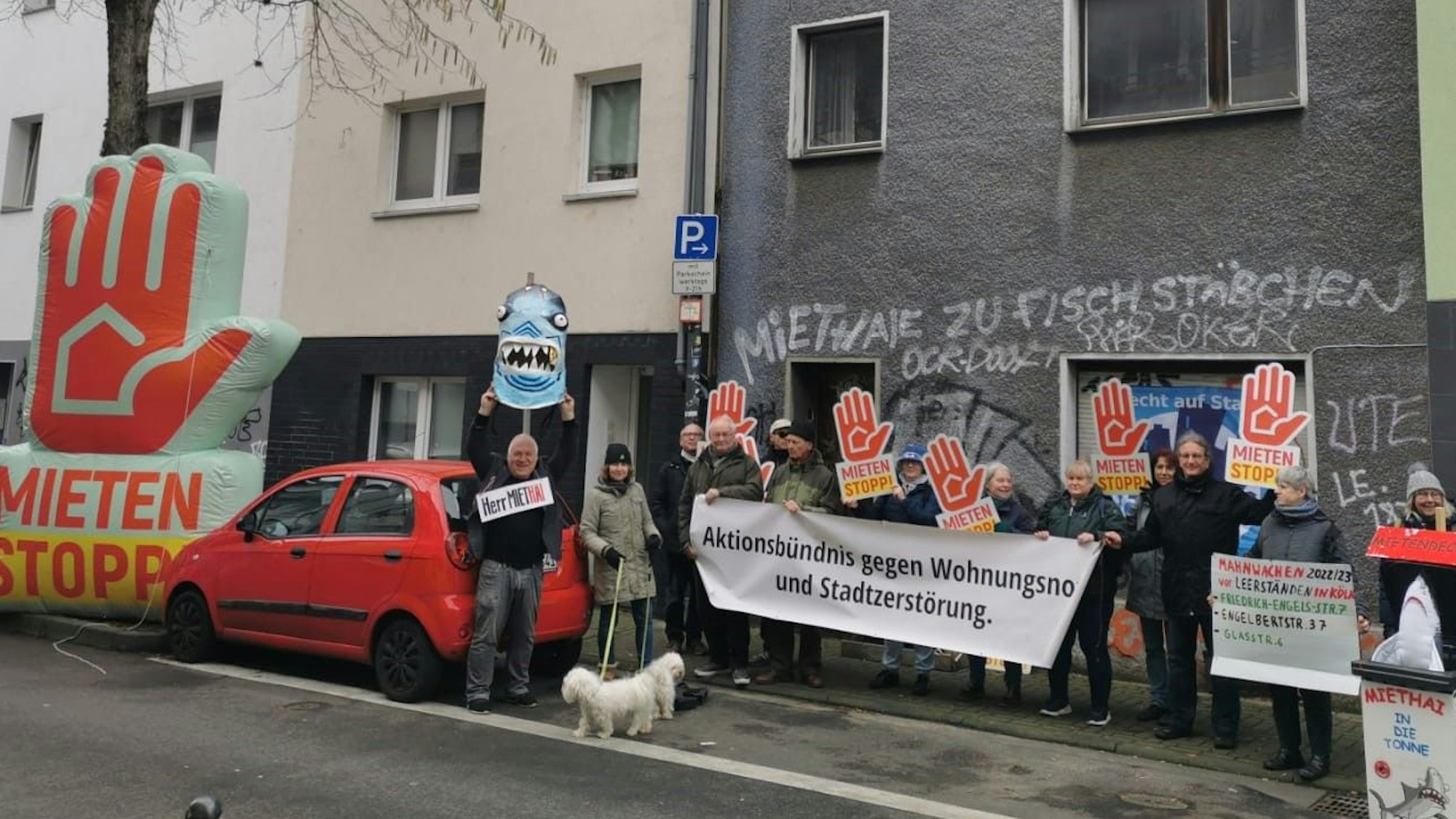 Männer und Frauen haben sich vor einem leerstehenden Haus positioniert. Einige halten ein Transparent mit der Aufschrift „Aktionsbündnis gegen Wohnungsnot und Stadtzerstörung“, andere Plakate mit der Forderung „Mieten Stopp“.