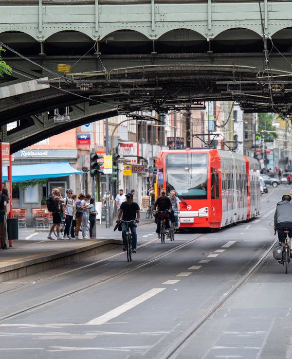 Eine KVB-Bahn der Linie fährt durch eine Unterführung am Bahnhof Süd. Vor der Bahn sind einige Radfahrende unterwegs.
