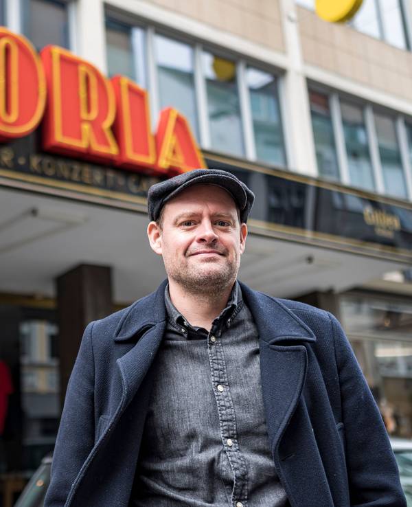 Komiker Max Giermann steht vor dem Gloria in Köln und lacht in die Kamera.