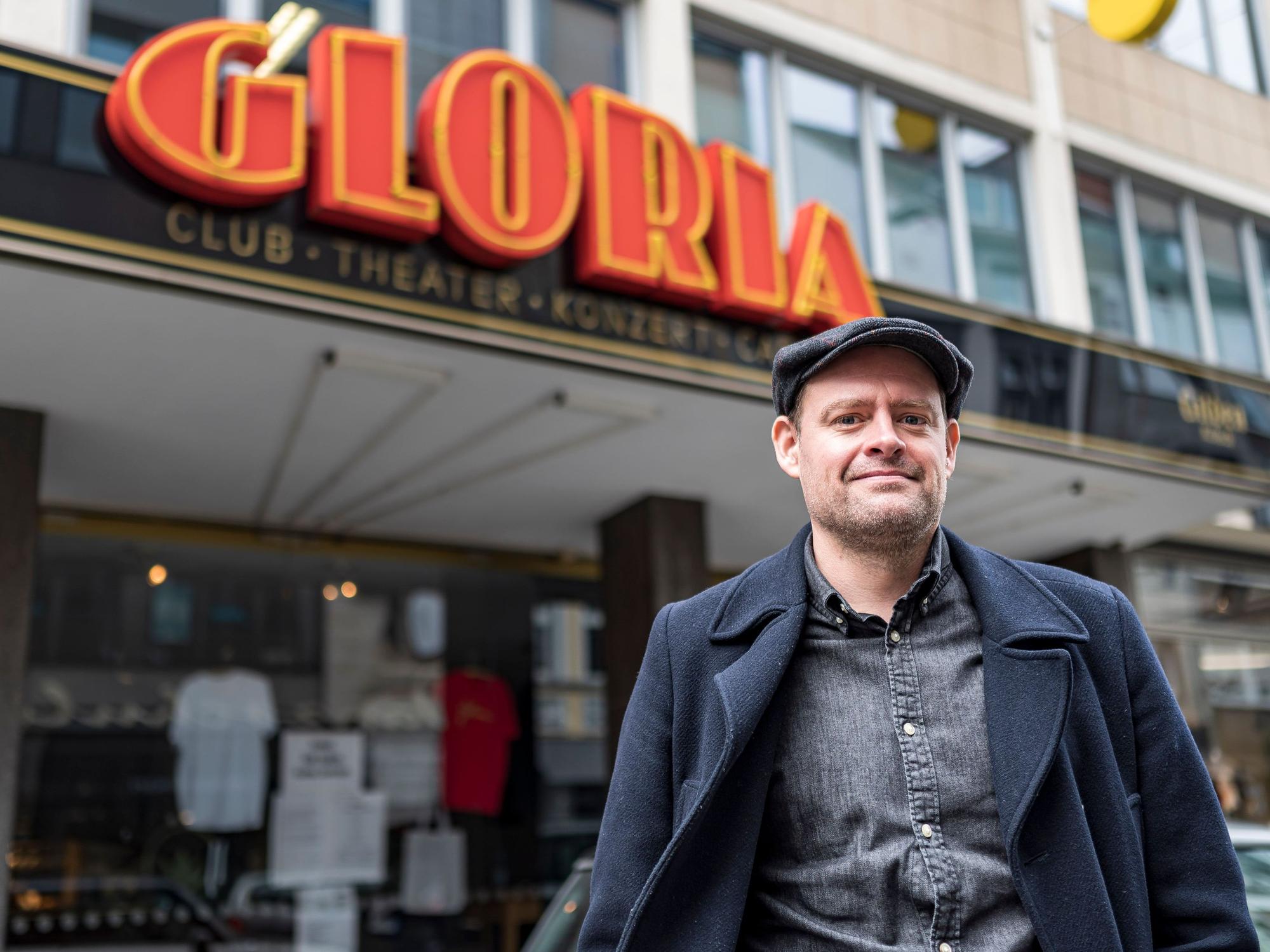Komiker Max Giermann steht vor dem Gloria in Köln und lacht in die Kamera.