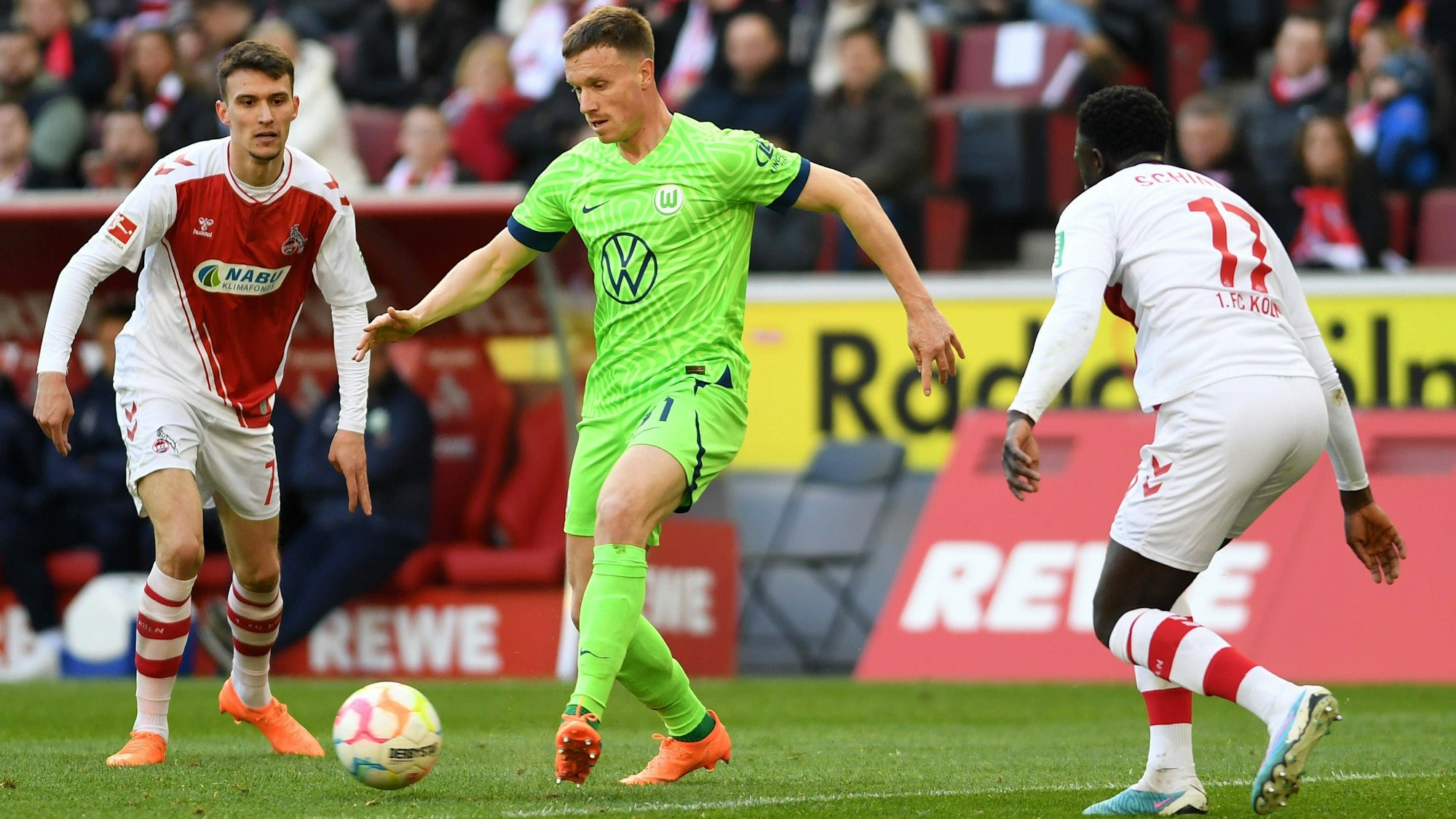 Yannick Gerhardt (M.) wird beim Bundesliga-Spiel 1. FC Köln gegen VfL Wolfsburg am Samstag (25. Februar 2023) von Dejan Ljubicic (l.) und Kingsley Schindler umringt.