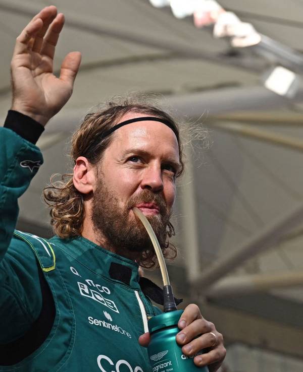 Sebastian Vettel trinkt und winkt dabei im Rennanzug von Aston Martin den Fans zu.