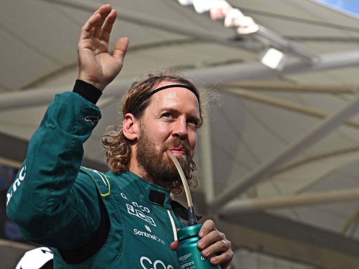 Sebastian Vettel trinkt und winkt dabei im Rennanzug von Aston Martin den Fans zu.