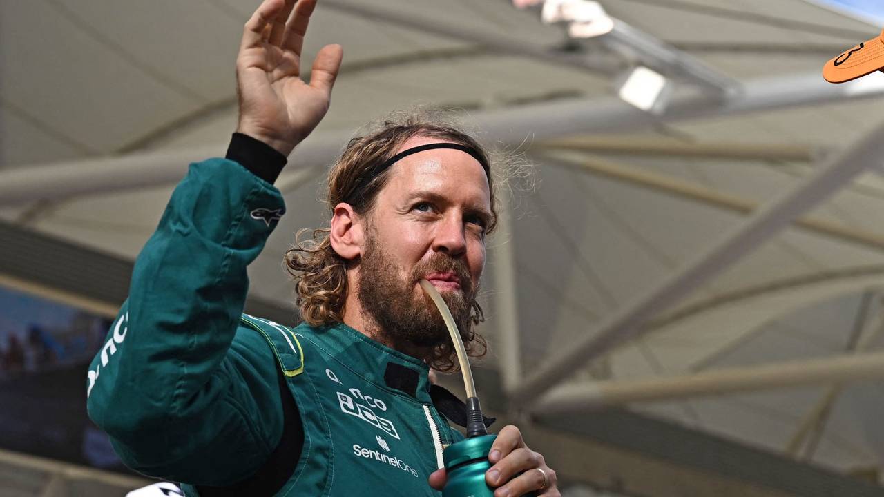 Sebastian Vettel trinkt und winkt dabei im Rennanzug von Aston Martin den Fans zu.