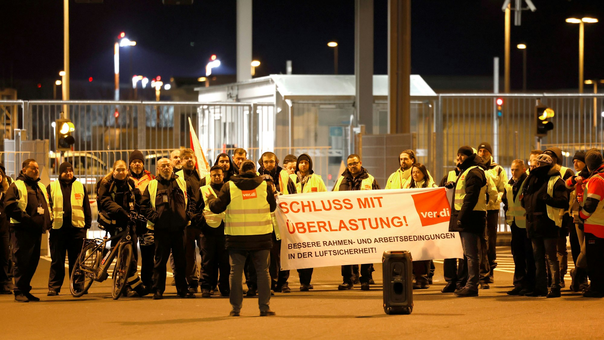 Streikende in Warnkleidung halten ein Banner der Gewerkschaft Verdi mit der Aufschrift: „Schluss mit Überlastung!“.