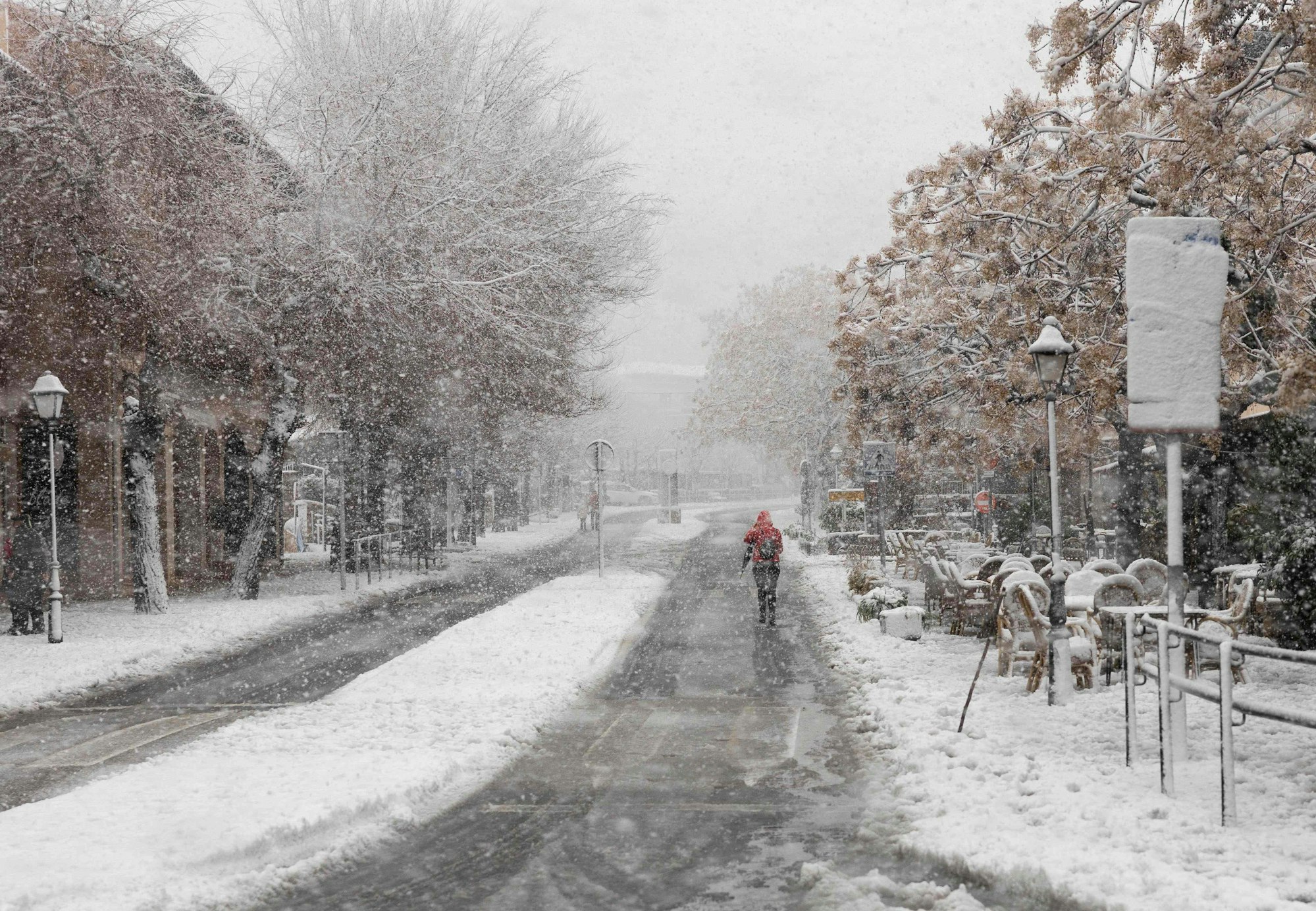 Eine Frau in einer roten Regenjacke läuft über eine verschneite Straße.