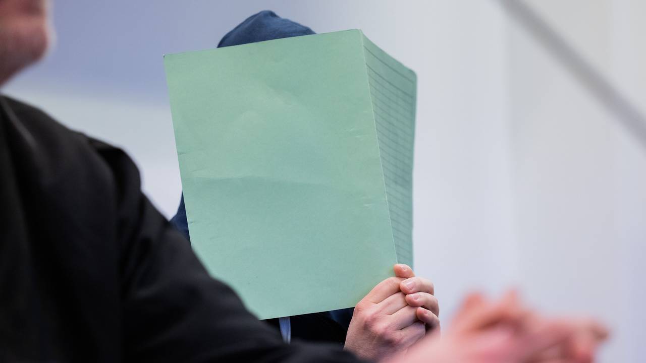 Der Angeklagte im Missbrauchskomplex Wermelskirchen hält sich im Gerichtssaal neben seinem Rechtsanwalt Christian Lange eine Mappe vor das Gesicht.