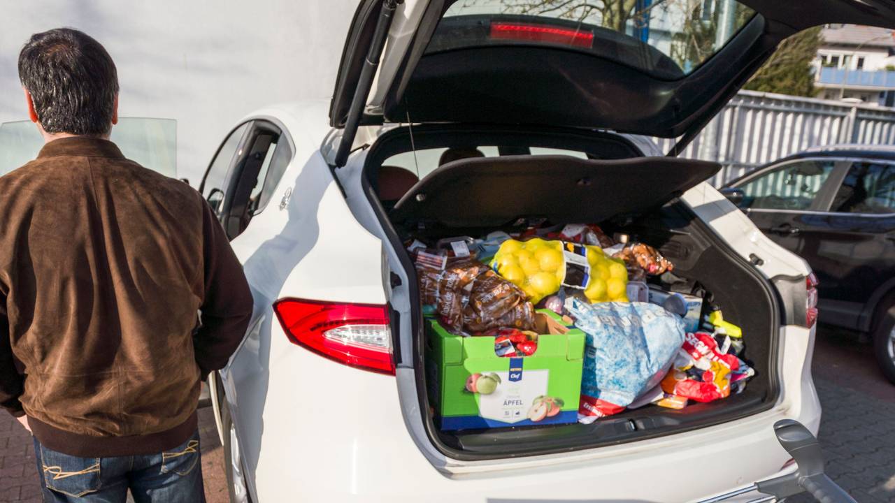 Ein Mann steht nach seinem Einkauf bei einem Discounter neben seinem vollen Einkaufswagen und dem bereits mit Lebensmitteln gut gefüllten Kofferraum seines Autos.