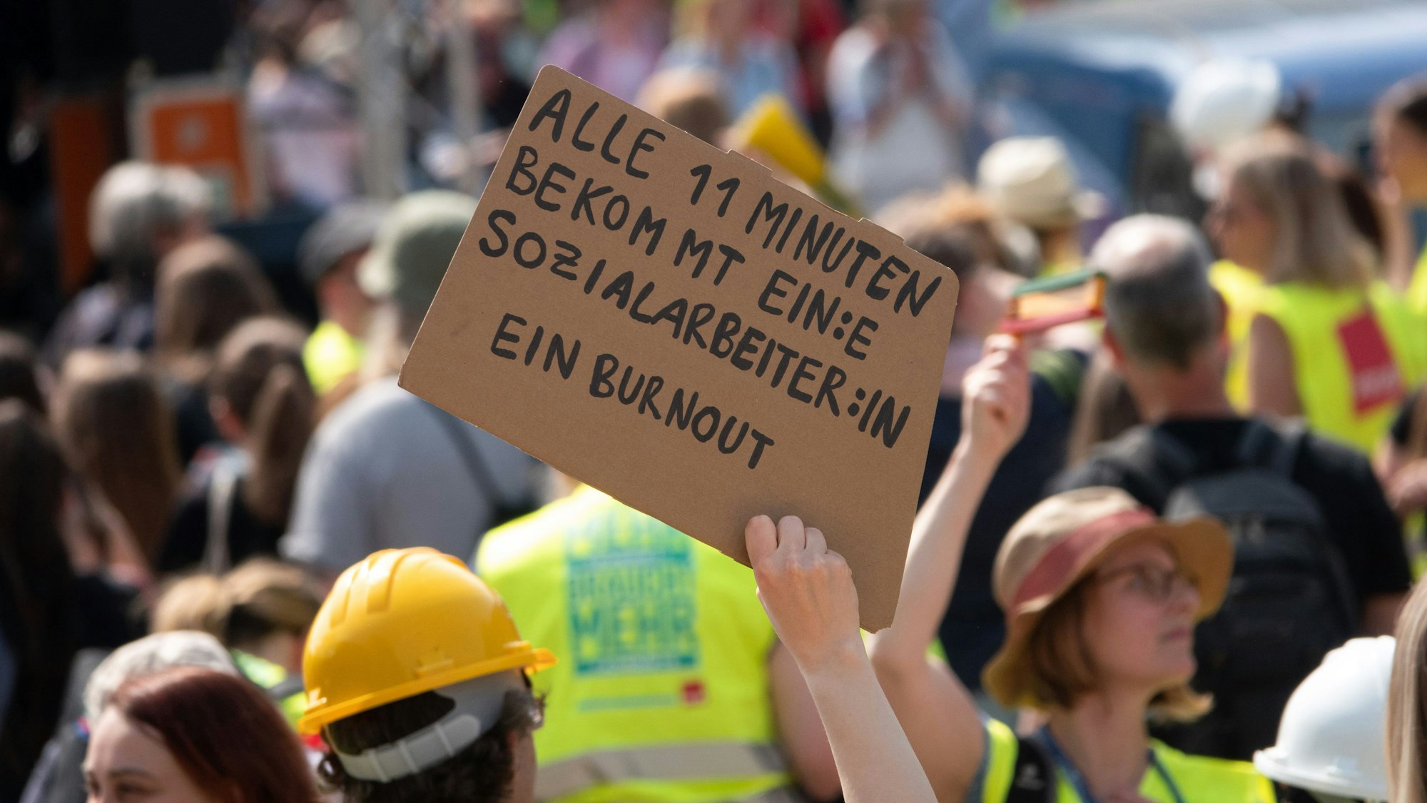 Eine Frau hält ein Schild mit der Aufschrift „Alle 11 Minuten bekommt ein:e Sozialarbeiter:in ein Burnout“ auf einer Kundgebung mehrerer Gewerkschaften auf dem Opernplatz in Hannover.
