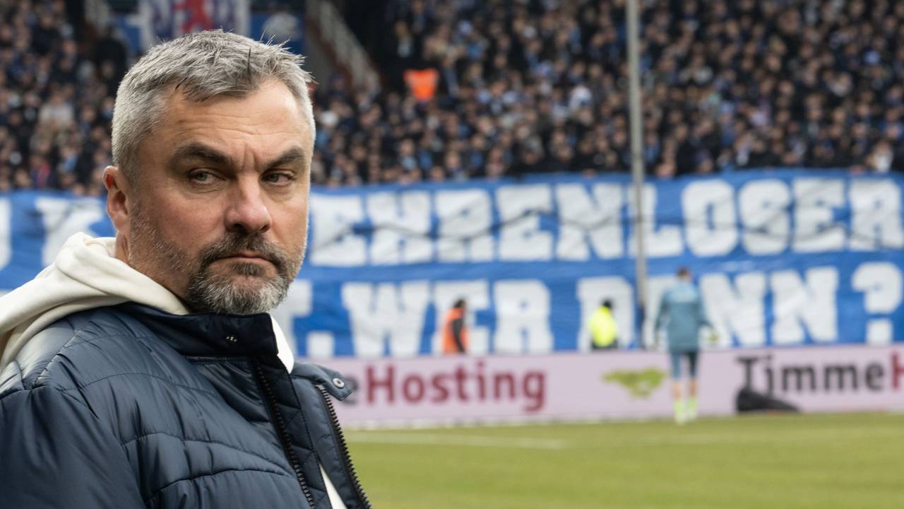 Thomas Reis steht bei seiner Rückkehr ins Ruhrstadion des VfL Bochum am Spielfeldrand. Im Hintergrund hängt ein beleidigendes Plakat gegen den Trainer von Schalke 04.