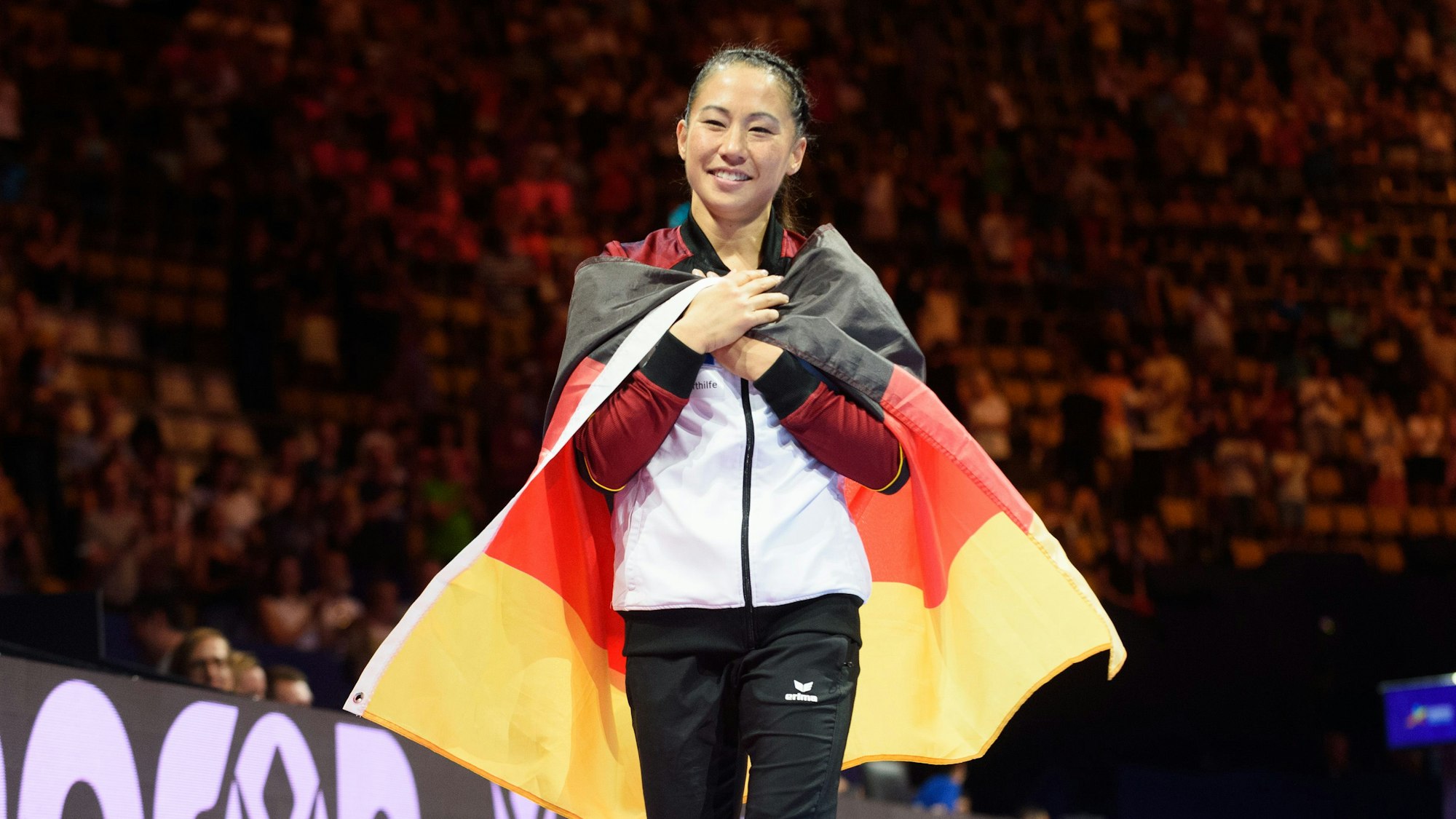 Kim Bui verabschiedet sich vom Leistung-Turnen und vom Publikum. Über den Schultern trägt sie eine Deutschland-Flagge.