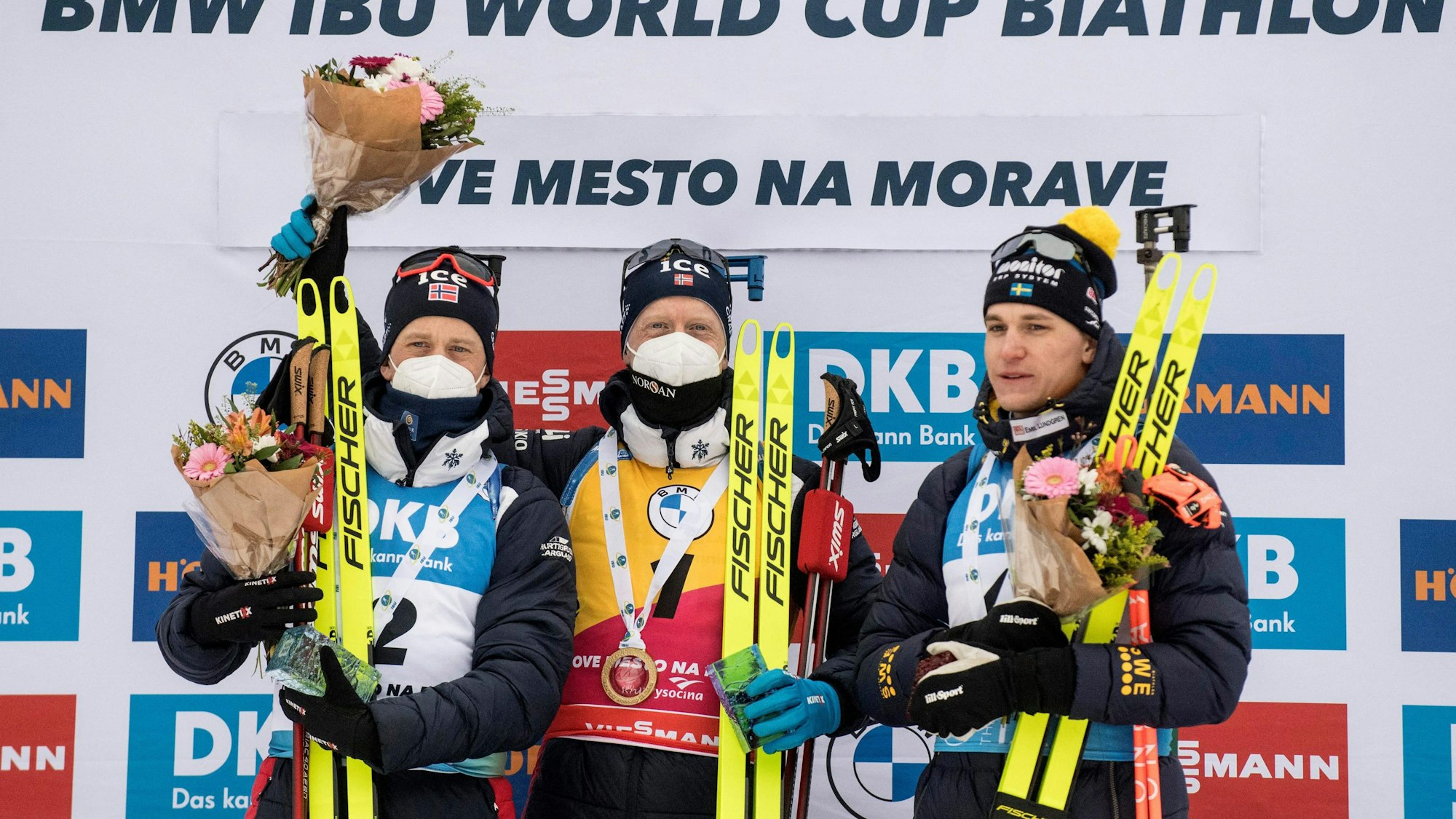 Johannes Thingnes Bö und sein Bruder Tarjei stehen bei der Siegerehrung neben Martin Ponsiluoma. Beide tragen einen Mund-Nasen-Schutz.