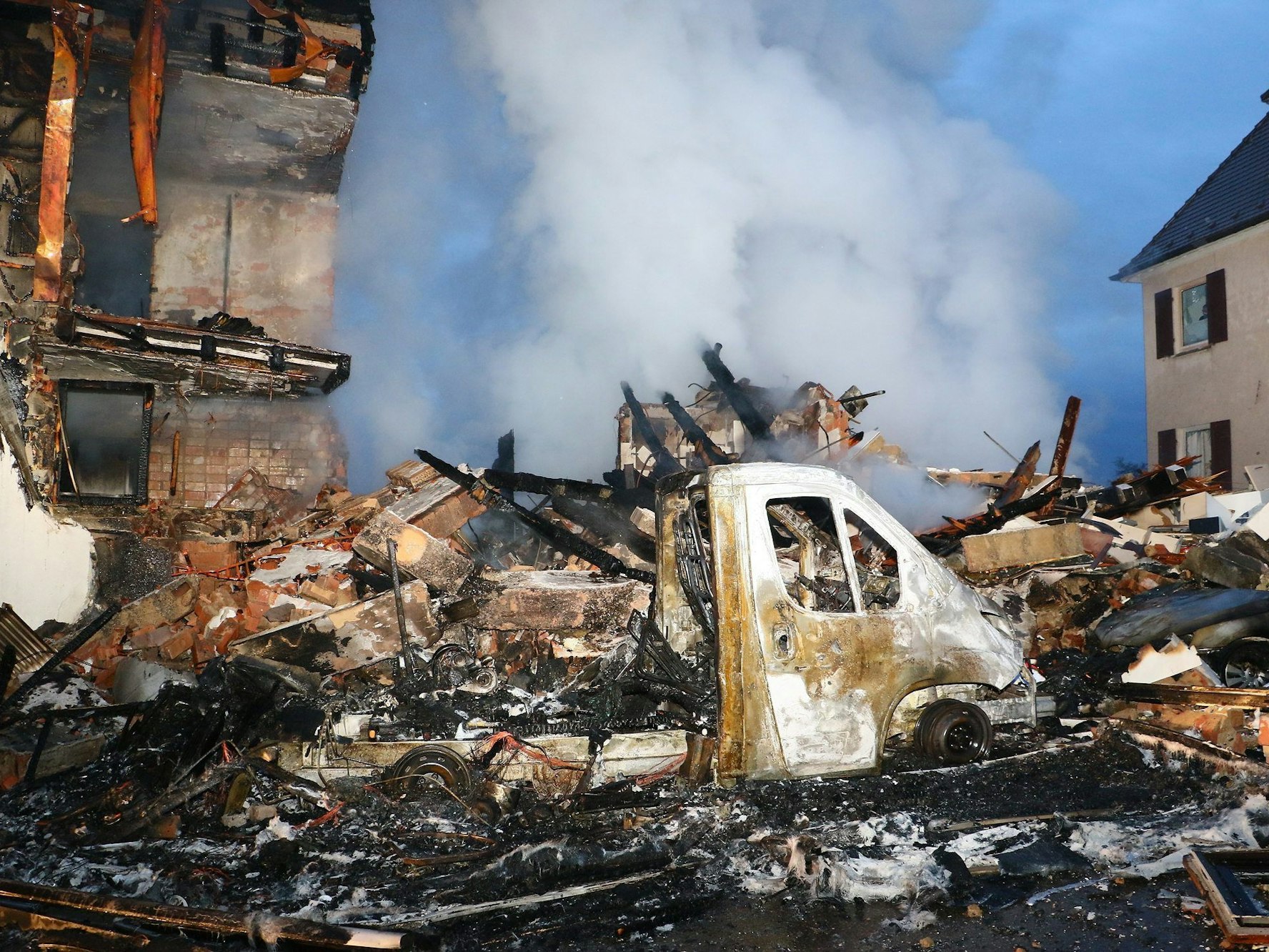 Ein ausgebrannter Kleinlaster steht in Stuttgart am Montag (6. März) vor den Trümmern eines Hauses. Nach einer Explosion wird ein Anwohner vermisst.