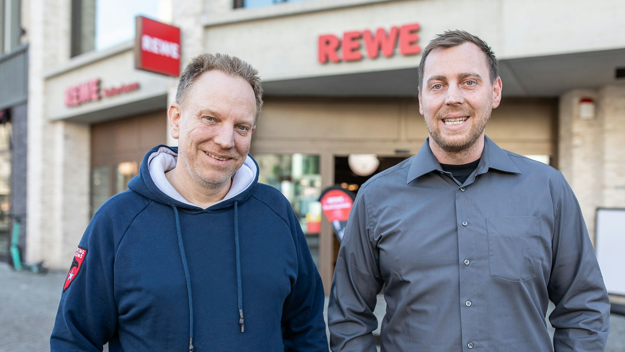 Zwei Männer stehen vor einem neuen Rewe in Köln. Dort wurde ein Teil der historischen Stadtmauer gefunden.