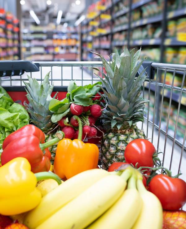 Ein Einkaufswagen mit Obst und Gemüse steht in einem Supermarkt.