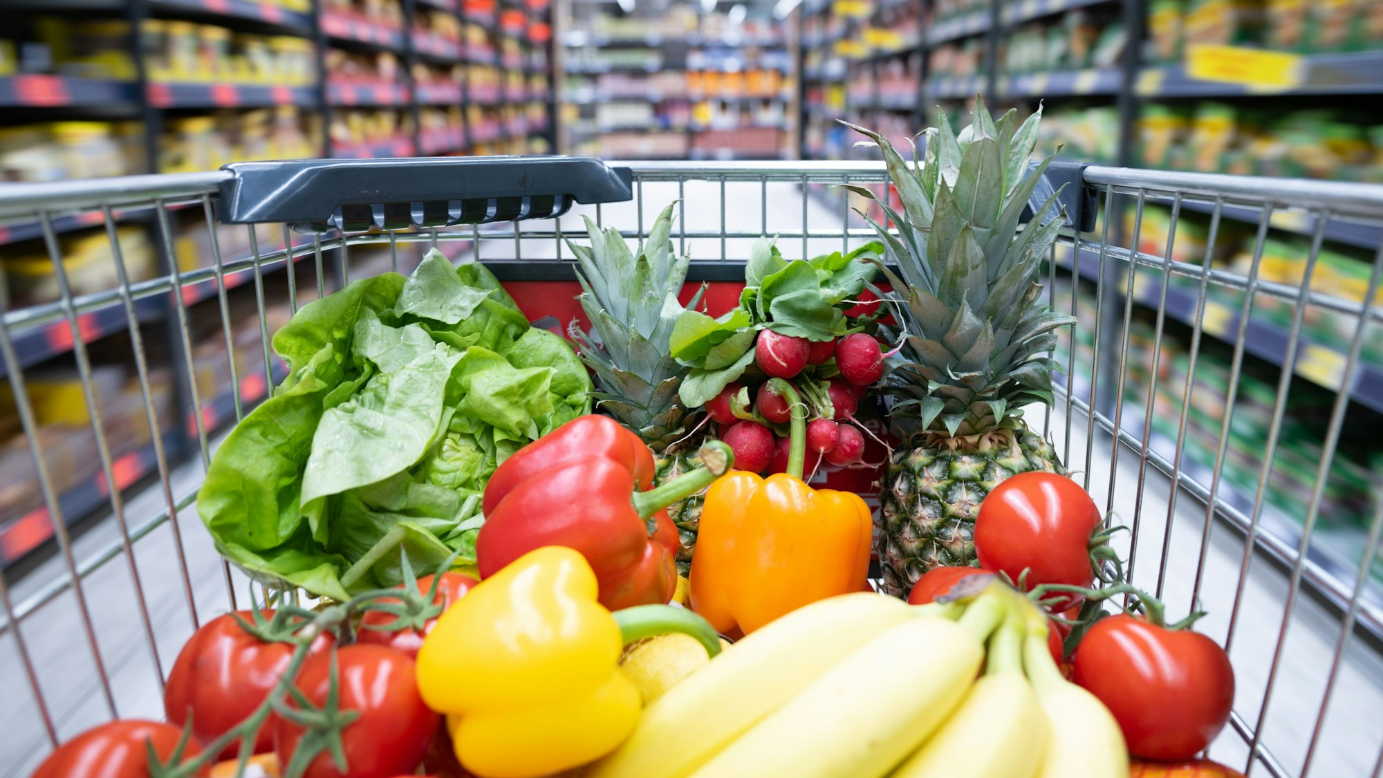 Ein Einkaufswagen mit Obst und Gemüse steht in einem Supermarkt.