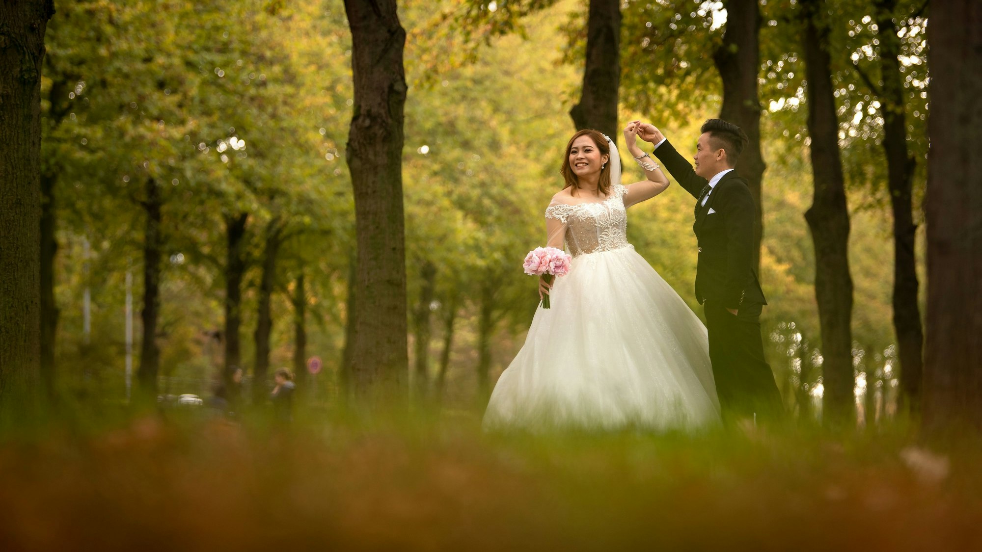 Ein Hochzeitspaar posiert in einer Allee für Fotos.