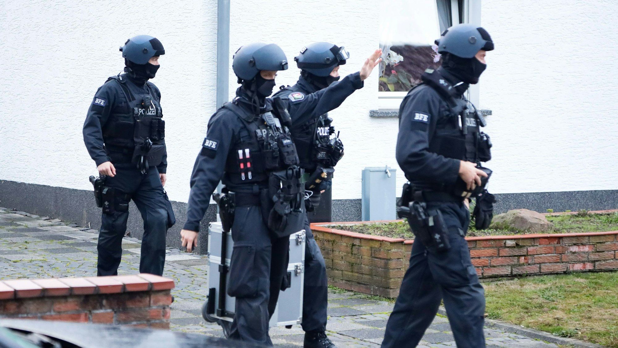 Maskierte Polizeikräfte gehen bei einer Razzia in Köln aus einem Haus heraus.