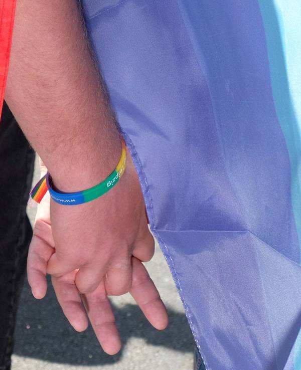 Das Symbolfoto zeigt zwei Teilnehmende der Demonstration zum Christopher-Street-Day (CSD). Sie tragen Fahnen und Armbänder in Regenbogenfarben und halten sich an den Händen.