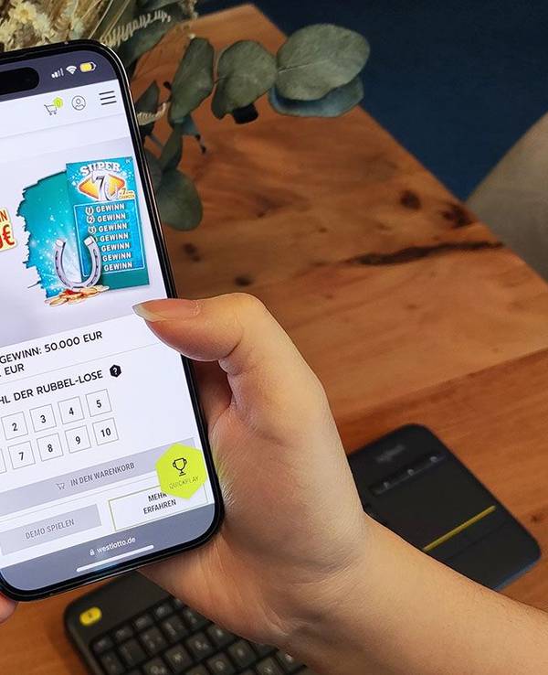 Weibliche Hand hält Smartphone in der Hand, auf dem WestLotto Rubbellose geöffnet sind.