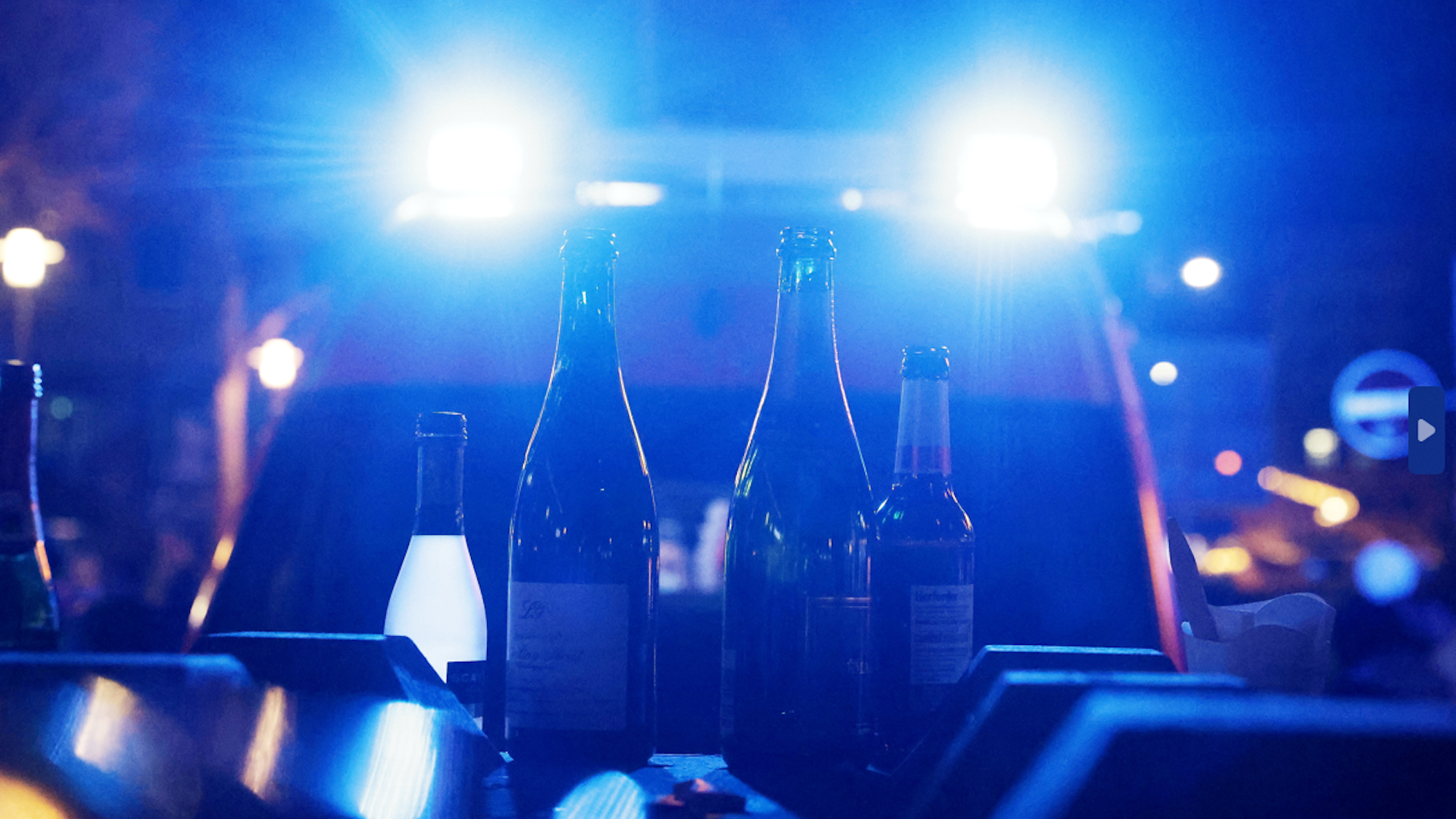 Leere Flaschen, die vorher mit alkoholischen Getränken gefüllt waren, stehen am Rheinufer vor einem Krankenwagen mit eingeschaltetem Blaulicht.