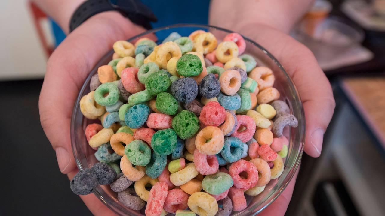 Das Symbolfoto aus dem Jahr 2018 zeigt eine Glasschüssel mit bunten, zu Ringen geformten Cornflakes. Die Schüssel wird von zwei Händen gehalten.