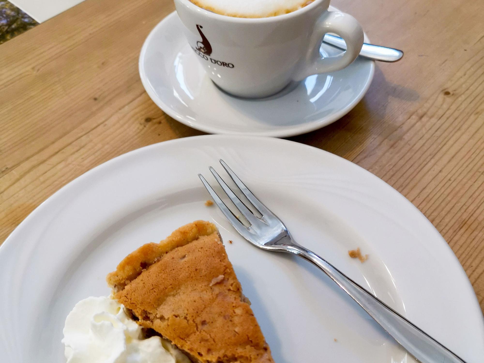 Ein Stück Kuchen und Sahne liegen mit einer Kuchengabel auf einem weißen Teller. Daneben steht eine Tasse Kaffee, aufgenommen im Oktober 2021 in Castasegna in der Schweiz.