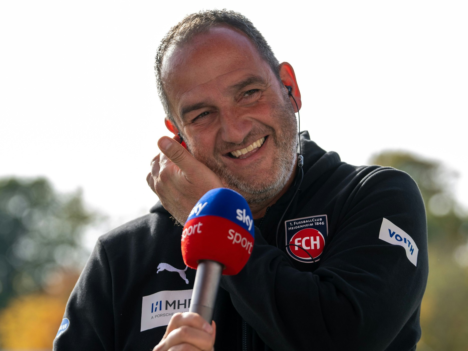 Heidenheims Trainer Frank Schmidt lacht am Sky-Mikrofon.