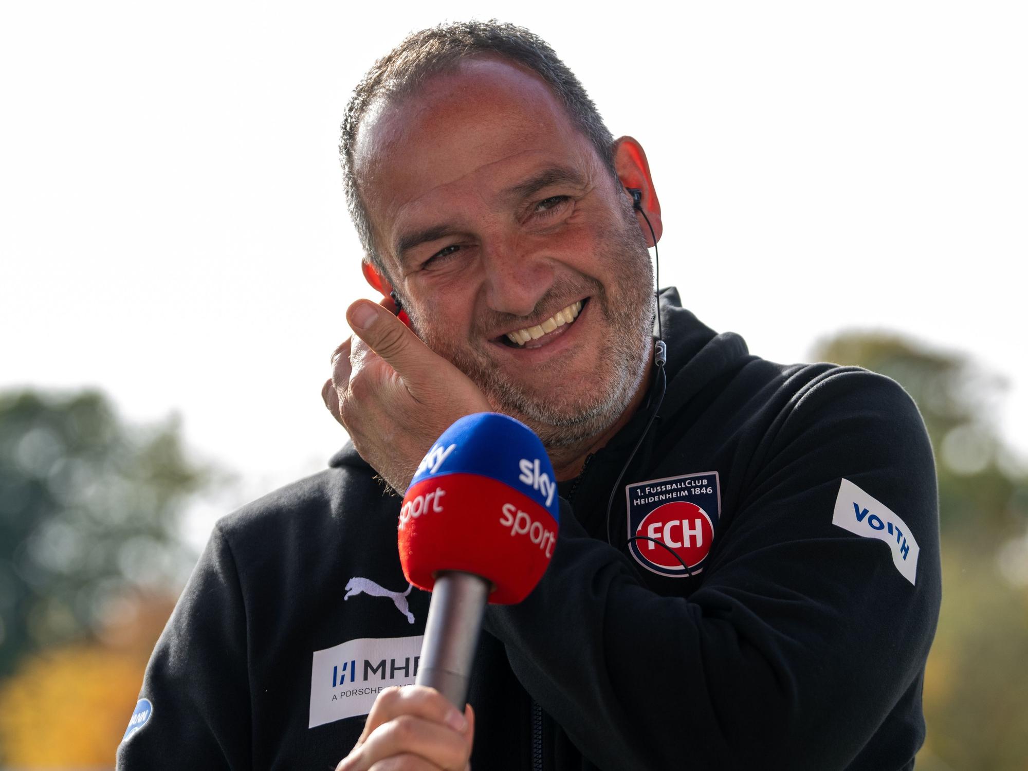 Heidenheims Trainer Frank Schmidt lacht am Sky-Mikrofon.