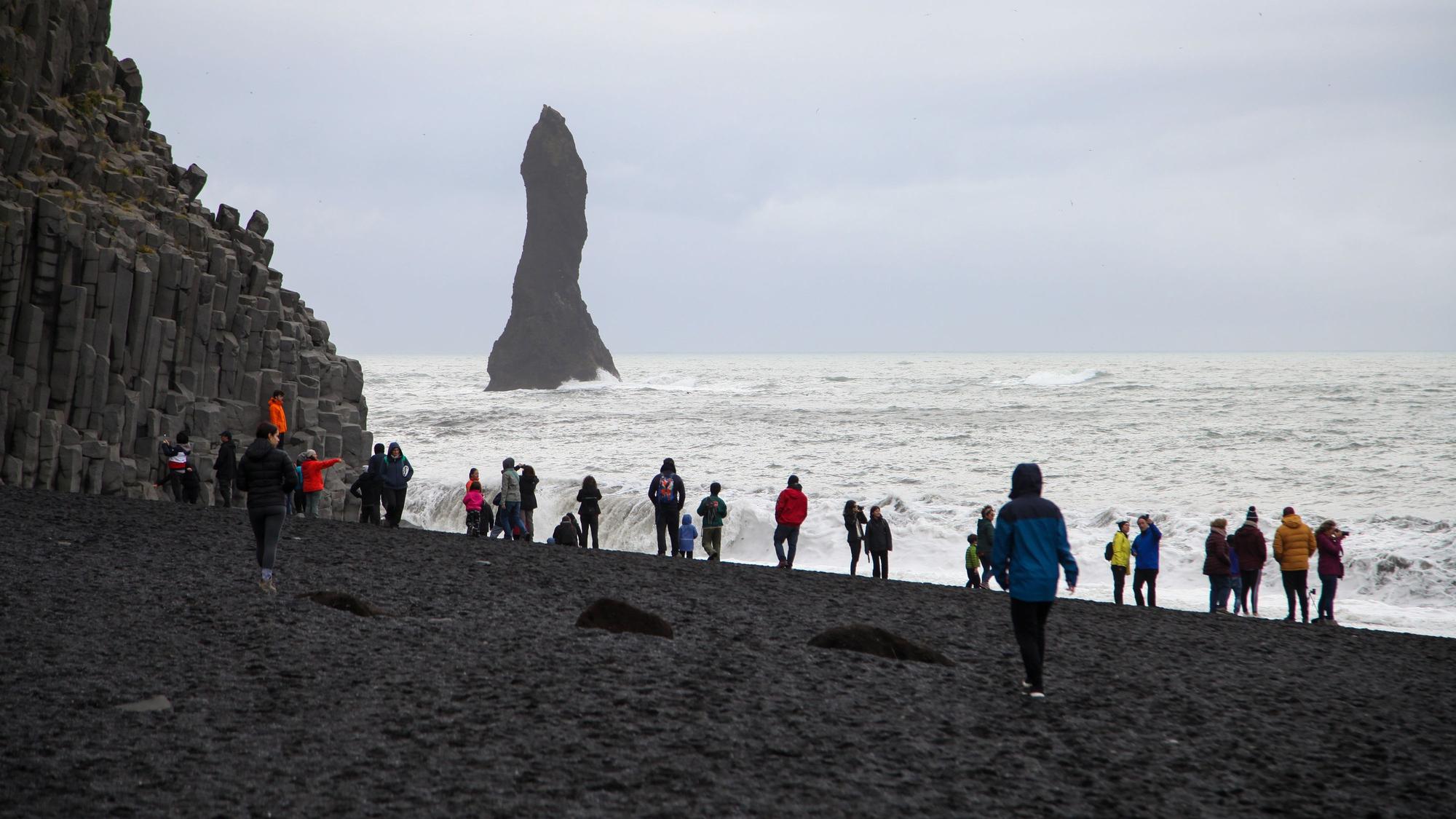 Touristinnen und Touristen spazieren über den schwarzen Strand Reynisfjara.