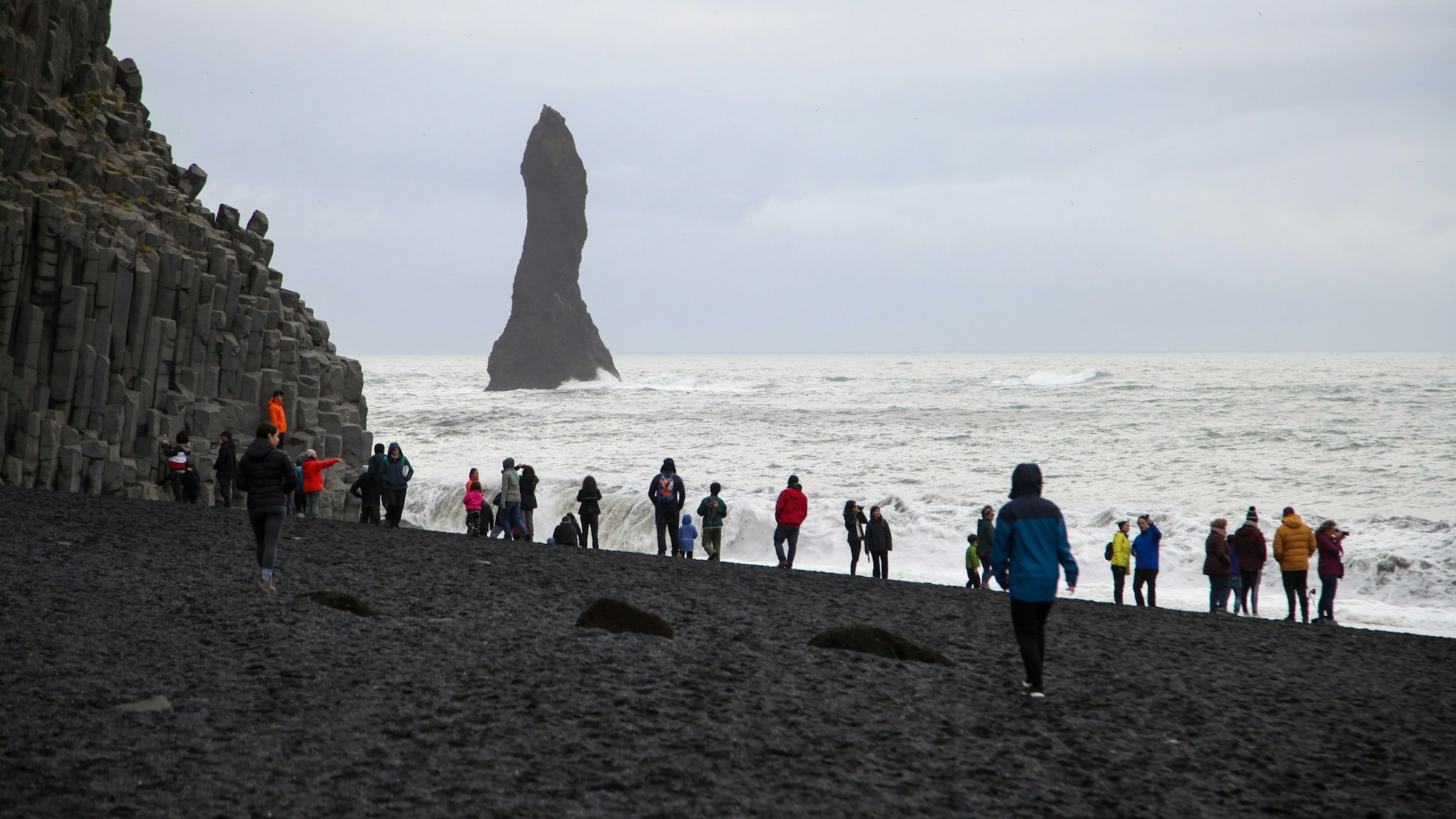 Touristinnen und Touristen spazieren über den schwarzen Strand Reynisfjara.