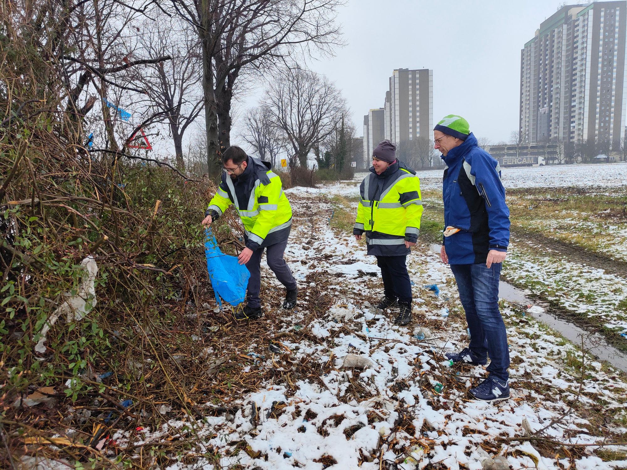 Hier pflücken drei städtische Mitarbeiter Plastikmüll aus den Sträuchern in Köln-Meschenich.
