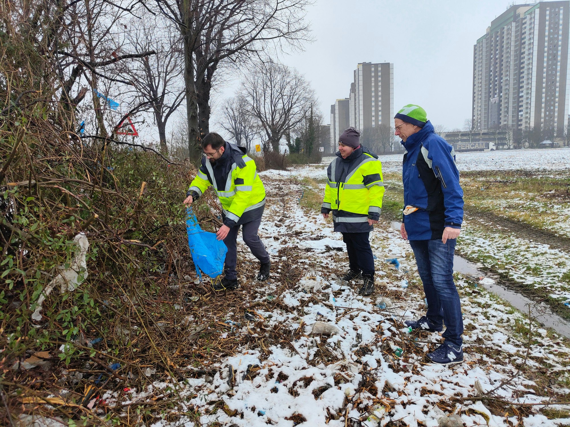 Hier pflücken drei städtische Mitarbeiter Plastikmüll aus den Sträuchern in Köln-Meschenich.