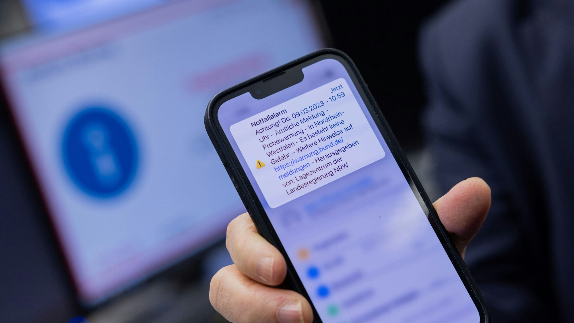 Herbert Reul zeigt sein Mobiltelefon, nachdem er den landesweiten Probealarm am Warntag per Mausklick im Lagezentrum der Landesregierung im Innenministerium ausgelöst hat.