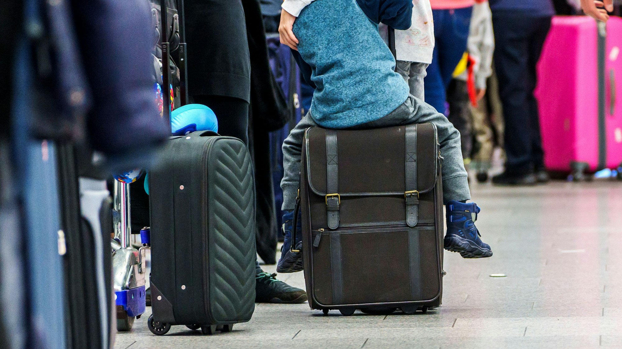 Ein Kind sitzt in einer Warteschlange am Flughafen in Frankfurt am Main auf seinem Koffer.