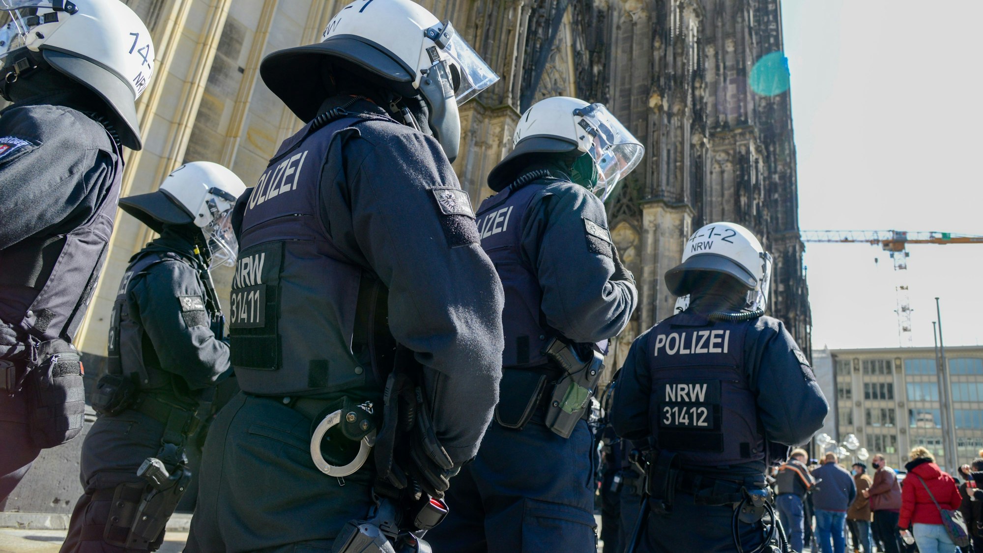 Polizeikräfte mit Schutzhelmen stehen vor dem Kölner Dom, wo mehrere Menschen demonstrieren.