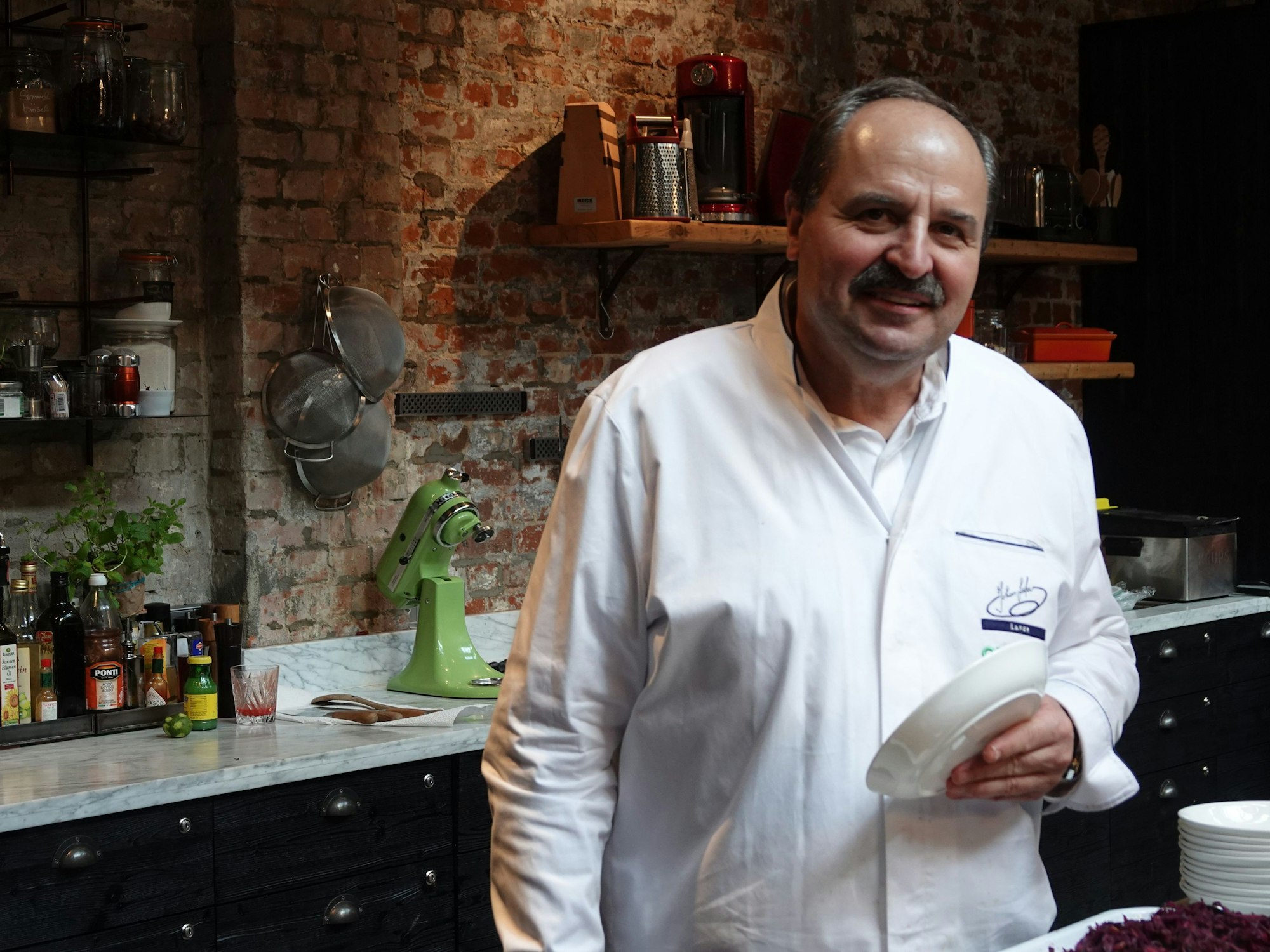 Der Fernsehkoch Johann Lafer hält einen Teller in der Hand bei einer Werbeveranstaltung des Unternehmens Groupon.