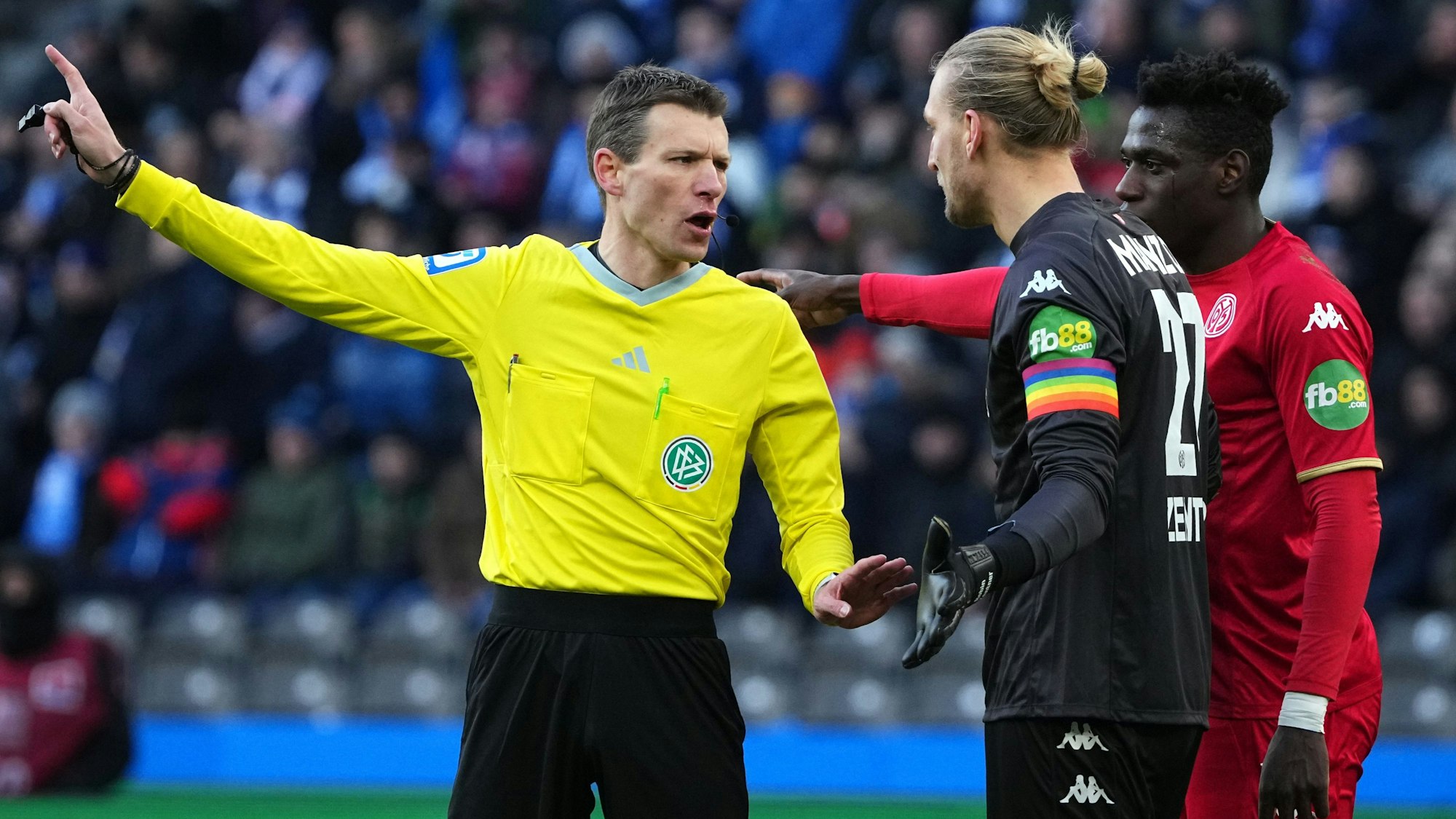 Schiedsrichter Benjamin Cortus (l) diskutiert in der ersten Halbzeit mit Torhüter Robin Zentner (M) von Mainz und dessen Teamkollegen Danny da Costa (r).